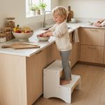 Toddler standing on white and natural wood 2-step stool in kitchen